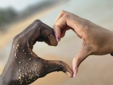Photo by Emmanuel Anderson Two hands reaching out towards each other on a beach